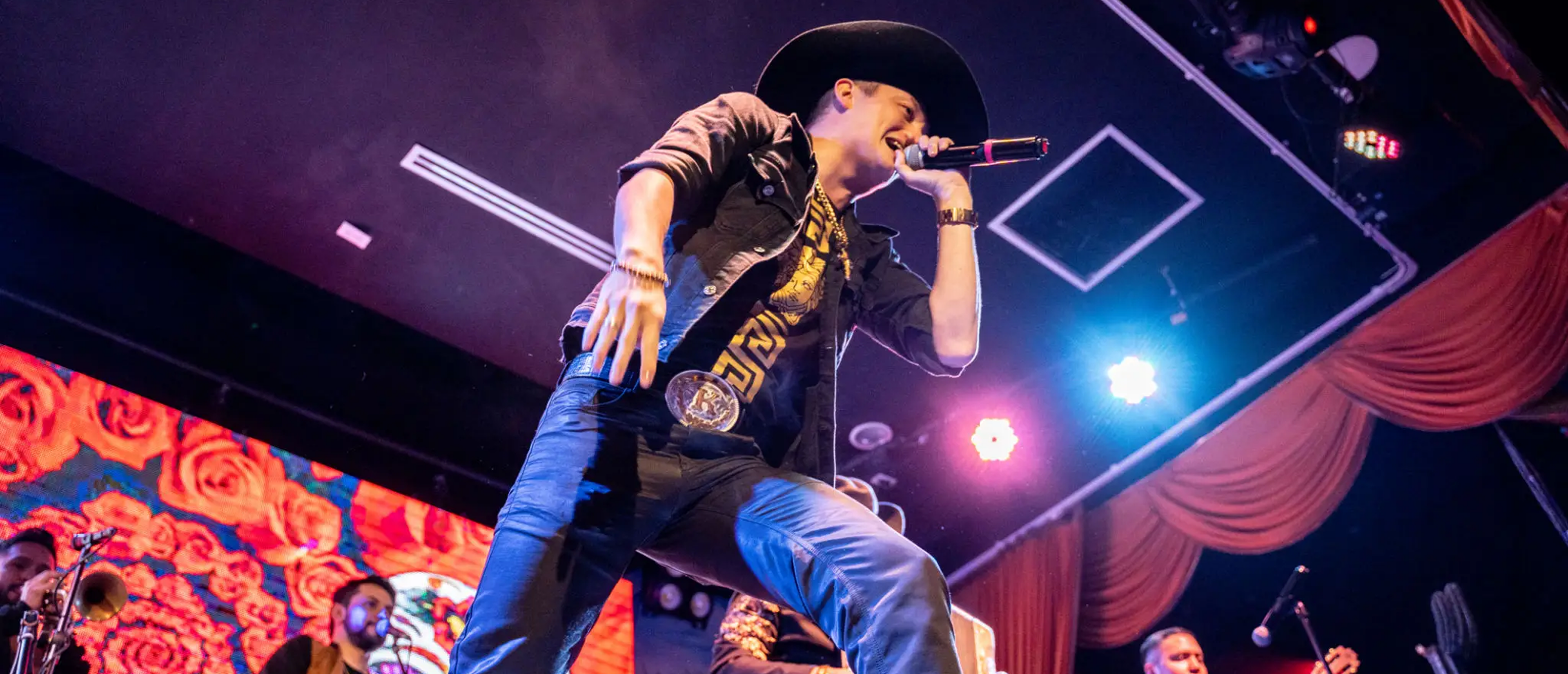Singer wearing hat performing on colorfully lit stage